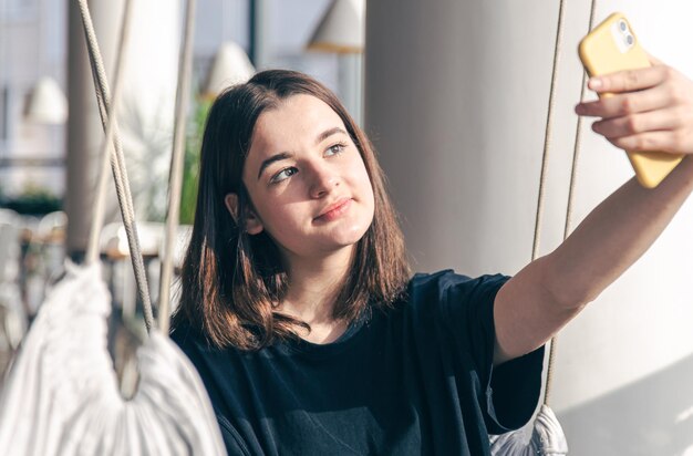 A teenager girl sits in a suspended hammock and takes a selfie on a smartphone