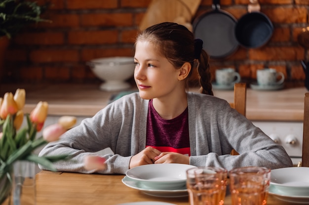 Ragazza dell'adolescente che si siede al tavolo da cucina. cucina in stile loft con pareti in mattoni e frigorifero rosso.