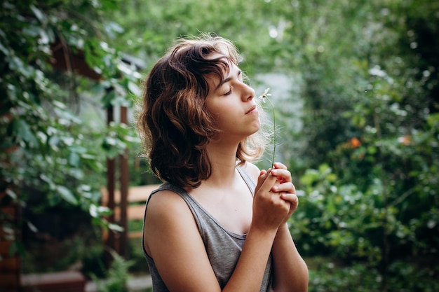 Adolescente ragazza che annusa il fiore di camomilla nella foresta. bellezza naturale. momenti schietti