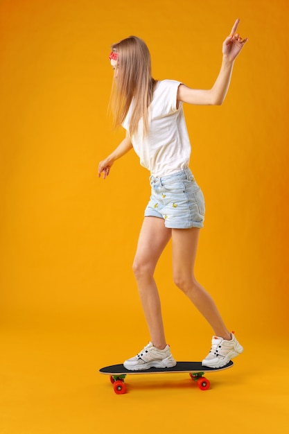 Teenager girl standing and posing on skateboard over a color background 