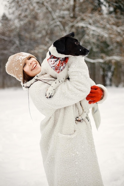 Девушка-подросток стоит в зимнем парке и держит черную собаку