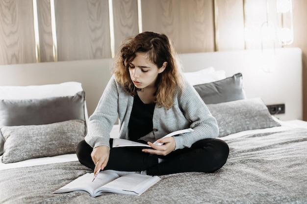 Девушка-подросток учится на кровати дома