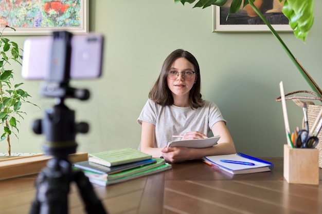 Teenager girl studying online using smartphone, female sitting at home at table with school books, listening talking at video conference. Distance learning, e-learning, technology, education, teens