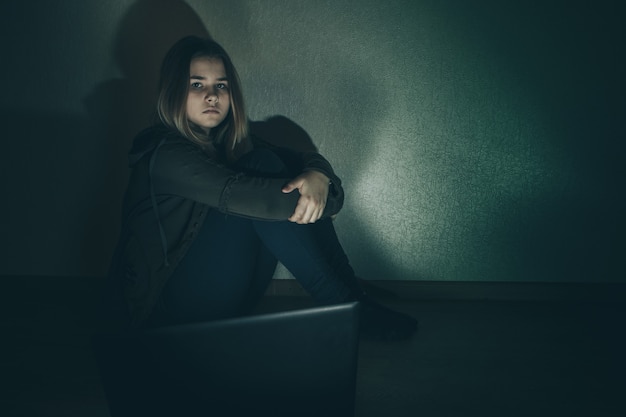 Teenager girl suffering internet cyber bullying scared and depressed cyberbullying. Image of despair girl humilated on internet by classmate. Young teenage girl crying in front of the laptop