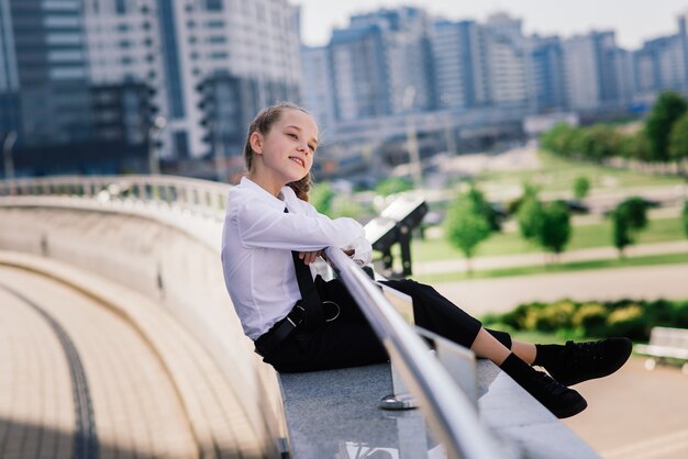 Teenager girl in summer in city park resting after school and college lessons, notebook in the hands.