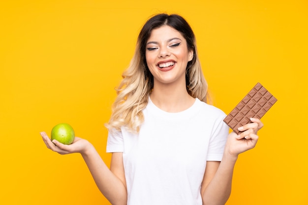 Teenager girl taking a chocolate tablet in one hand and an apple in the other