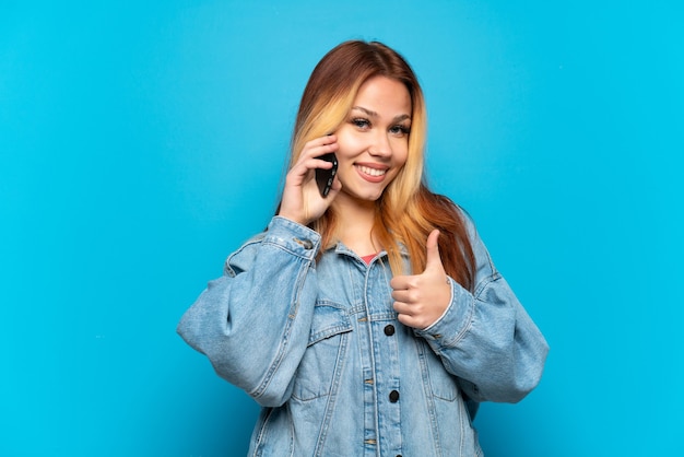 Teenager girl using mobile phone over isolated background giving a thumbs up gesture