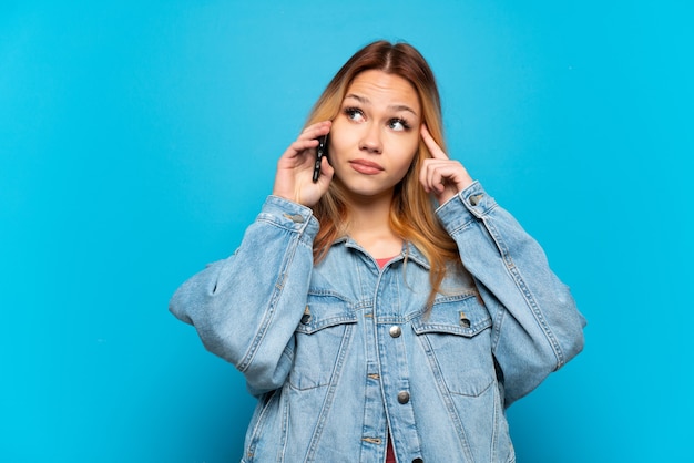 Teenager girl using mobile phone over isolated background having doubts and thinking