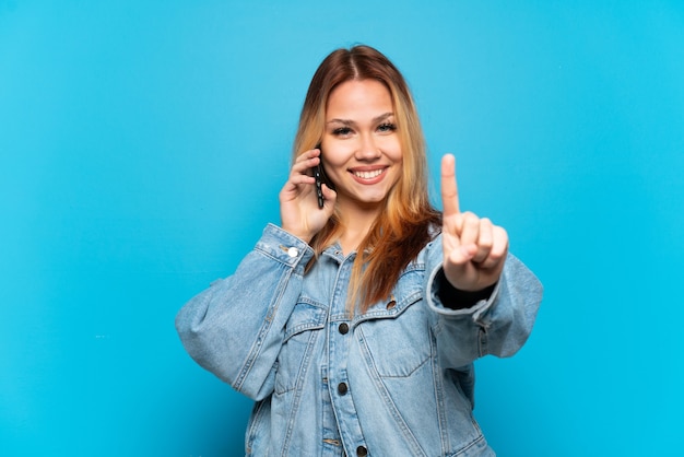 Teenager girl using mobile phone over isolated background showing and lifting a finger