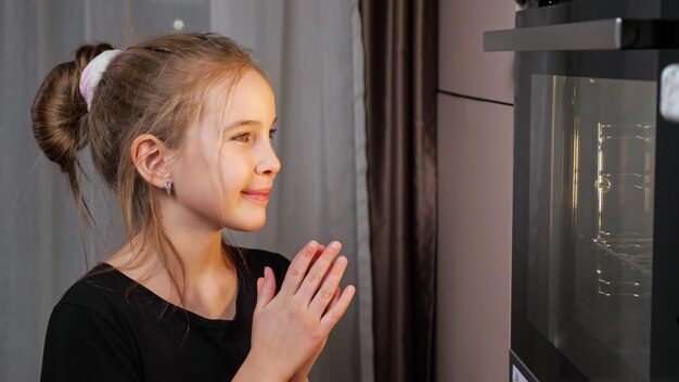 Teenager girl waits for food preparing in stove at home