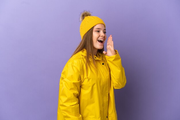 Teenager girl wearing a rainproof coat over isolated purple background shouting with mouth wide open to the side