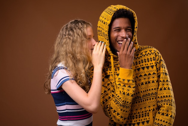 Teenager girl whispering to happy African man who is laughing