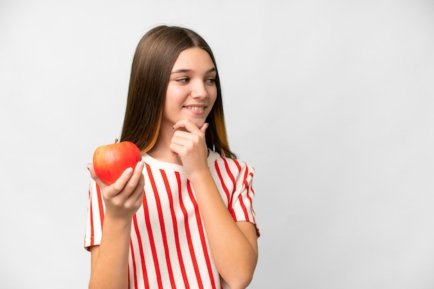 Foto ragazza adolescente con una mela su sfondo bianco isolato pensando un'idea e guardando il lato