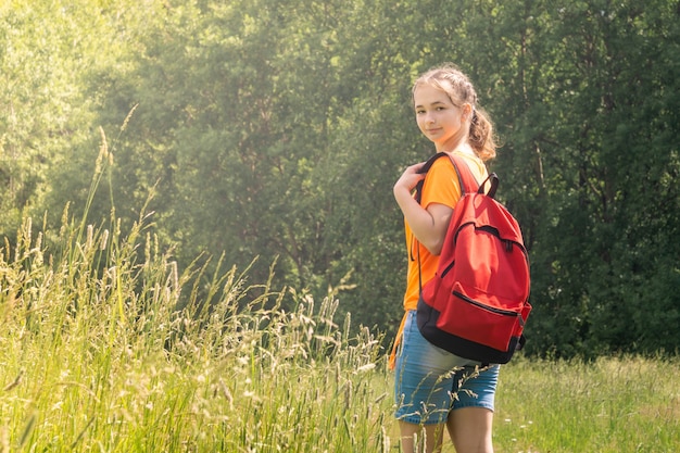 Teenager girl with backpack walks in a clearing in the woods