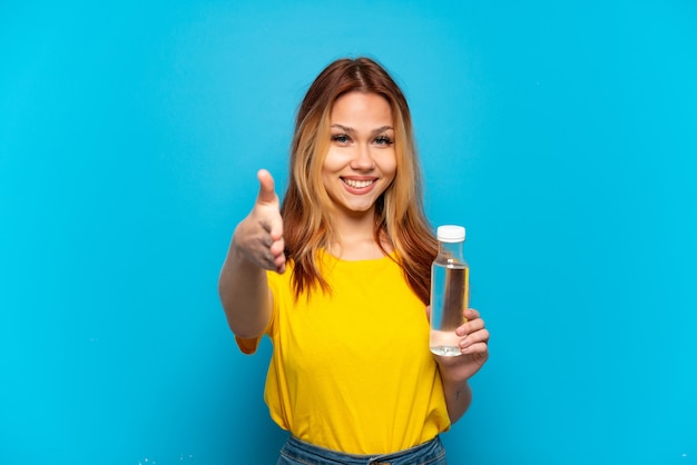 Teenager girl with a bottle of water over isolated blue background shaking hands for closing a good deal