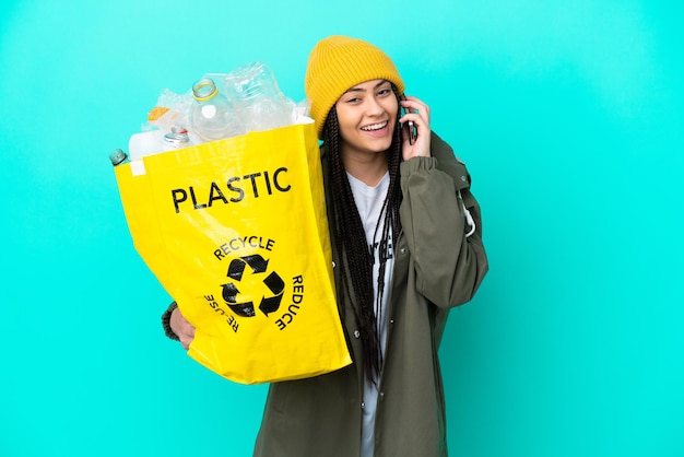 Teenager girl with braids holding a bag to recycle keeping a conversation with the mobile phone with someone