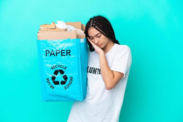 Teenager girl with braids holding a bag to recycle making sleep gesture in dorable expression