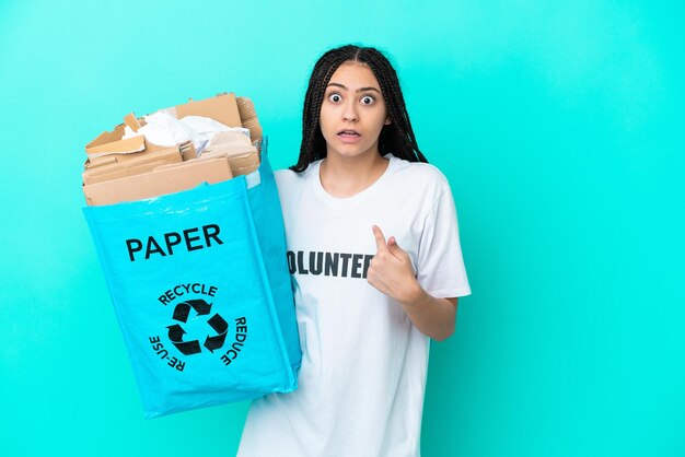 Teenager girl with braids holding a bag to recycle pointing to oneself