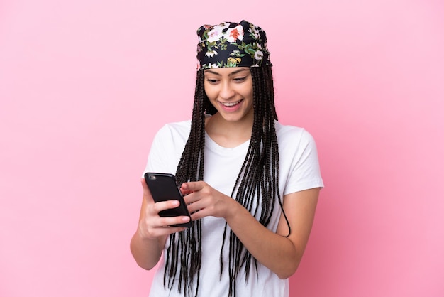 Teenager girl with braids over isolated pink background sending a message or email with the mobile