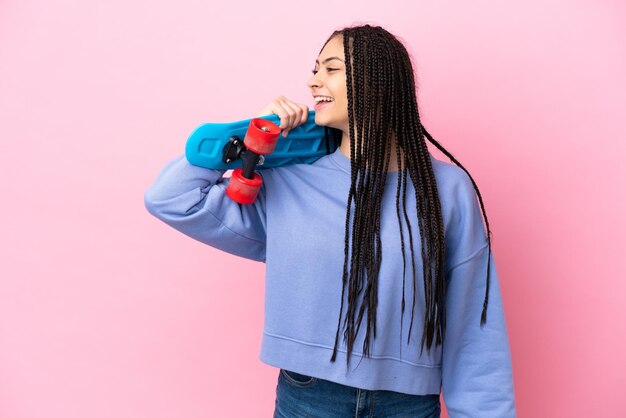 Teenager girl with braids over isolated pink background with a skate with happy expression