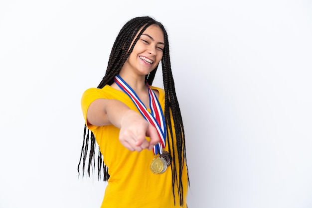 Teenager girl with braids and medals over isolated pink background points finger at you with a confident expression