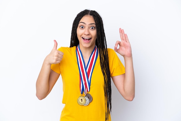 Teenager girl with braids and medals over isolated pink background showing ok sign and thumb up gesture