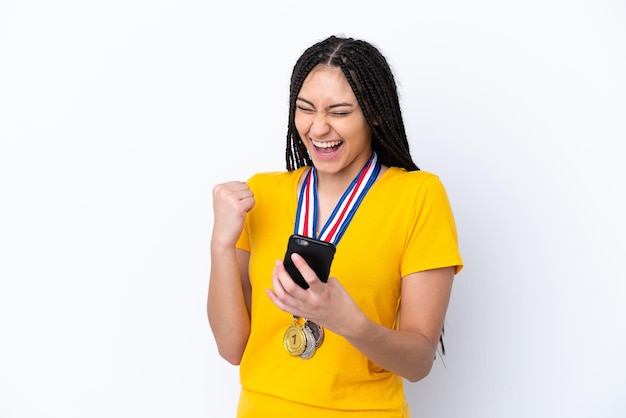 Teenager girl with braids and medals over isolated pink background with phone in victory position