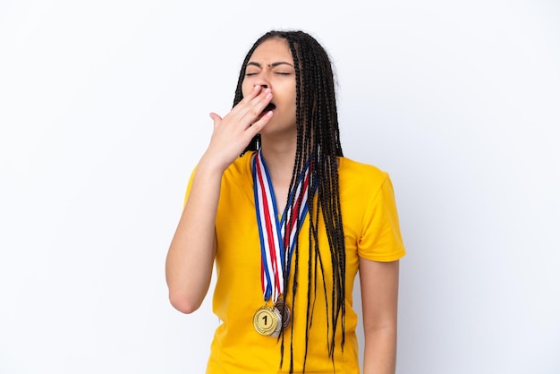 Teenager girl with braids and medals over isolated pink background yawning and covering wide open mouth with hand