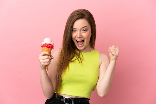 고립된 분홍색 배경 위에 코넷 아이스크림을 들고 우승자 위치에서 승리를 축하하는 10대 소녀