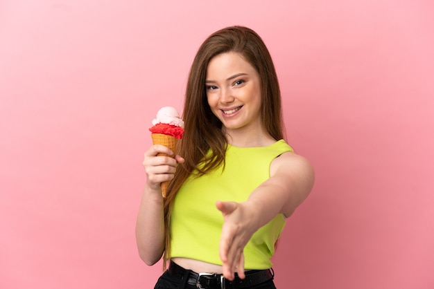 Ragazza adolescente con un gelato alla cornetta sul muro rosa isolato che stringe la mano per aver chiuso un buon affare