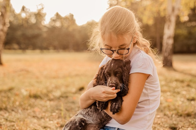 Teenager girl with glasses playing on grass with her little dog, brown cocker spaniel puppy, outdoors, in a park.