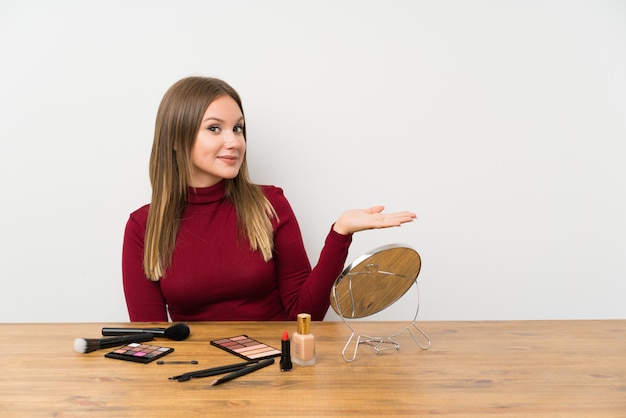 Teenager girl with makeup palette and cosmetics in a table extending hands to the side