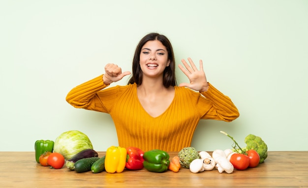 Teenager girl with many vegetables counting six with fingers