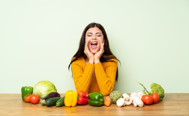 Teenager girl with many vegetables shouting and announcing something