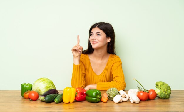 Ragazza dell'adolescente con molte verdure che mostrano e che alzano un dito nel segno del meglio