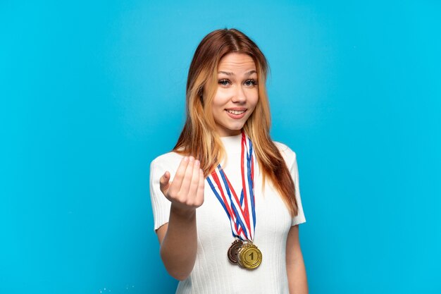 Teenager girl with medals over isolated background inviting to come with hand. Happy that you came