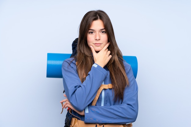 Teenager girl with a mountaineering backpack over blue wall