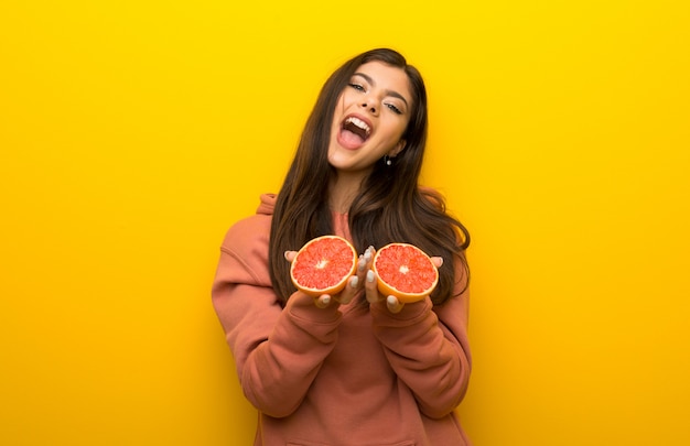 Teenager girl with pink sweatshirt on yellow background with oranges