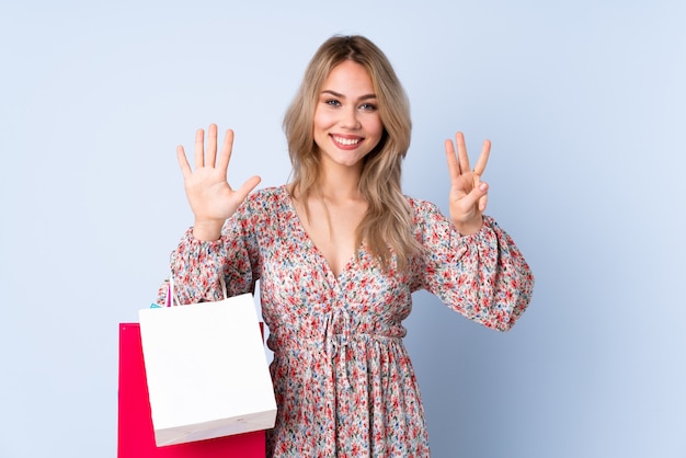 Teenager girl with shopping bag on blue wall counting eight with fingers