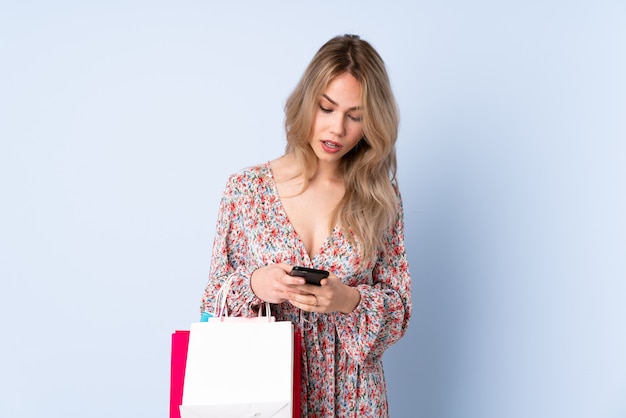 Teenager girl with shopping bag isolated on blue wall sending a message with the mobile