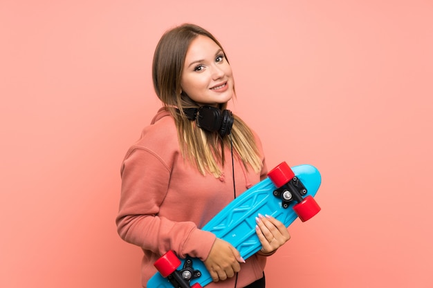 Teenager girl with skate over isolated pink wall