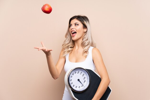 Teenager girl with weighing machine over isolated  with weighing machine and with an apple