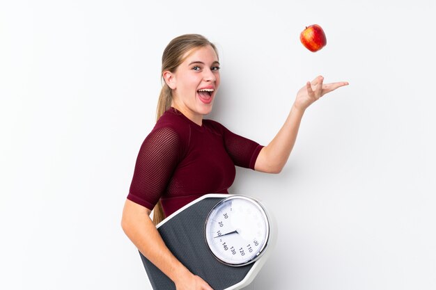 Teenager girl with weighing machine over white with weighing machine and with an apple