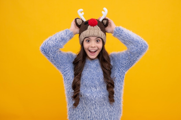 Teenager girl with winter hat over isolated yellow background\
winter christmas holidays new year mood kids warm clothes excited\
face cheerful emotions of teenager girl