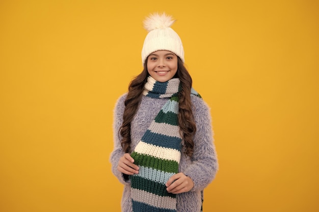 Teenager girl with winter hat over isolated yellow background\
winter christmas holidays new year mood kids warm clothes happy\
girl face positive and smiling emotions