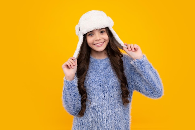 Teenager girl with winter hat over isolated yellow background\
winter christmas holidays new year mood kids warm clothes happy\
teenager positive and smiling emotions of teen girl