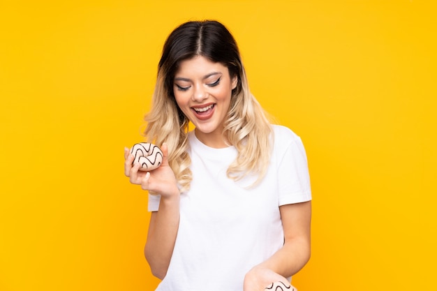 Teenager girl on yellow wall holding donuts with happy expression