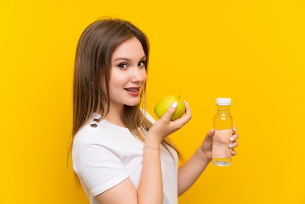 Teenager girl over yellow wall with an apple and a bottle of water