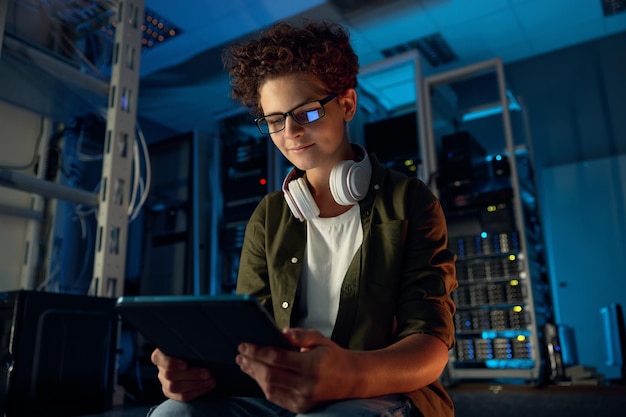 Teenager guy IT technician working on tablet in server room