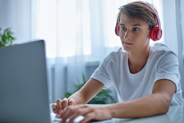 Teenager in headphones is working or teaching at home on his laptop